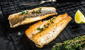 Pictured are cooked Branzino Fillets with skin on a rack with lemon and herb garnish.